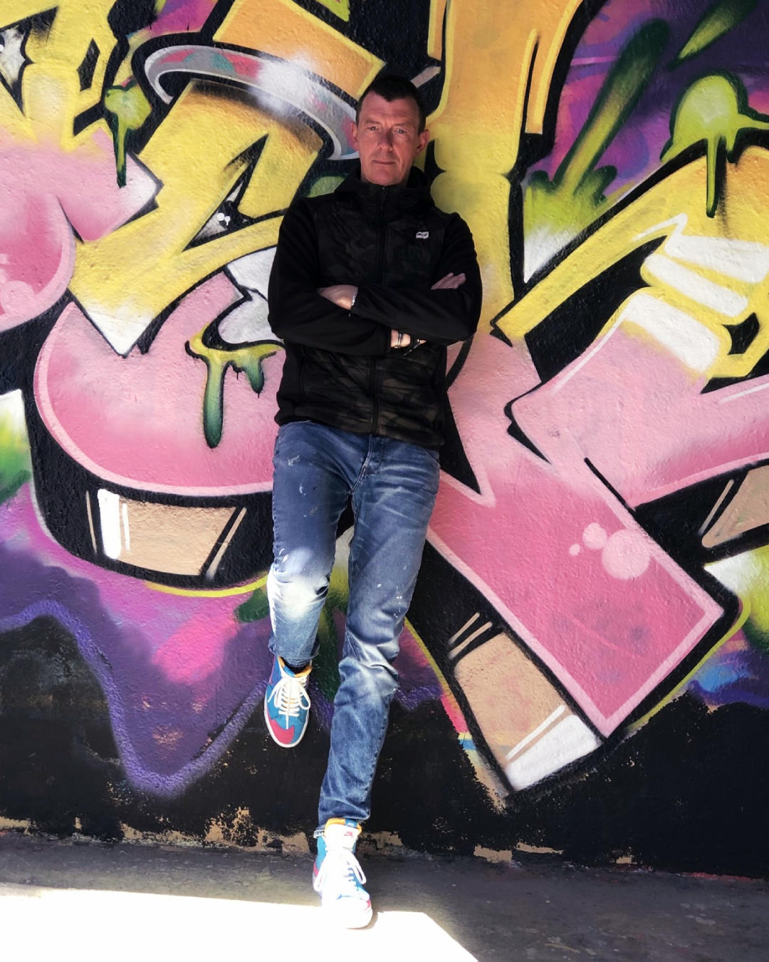 The founder standing in front of a colourful graffiti wall